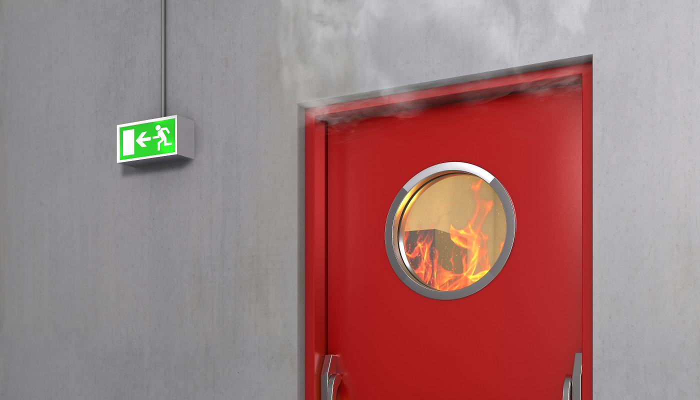 Smoke billowing out of a laboratory door, fire seen through the door's window.