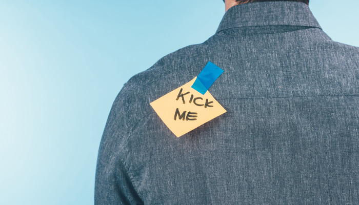 Note taped to back of man's shirt that reads "Kick Me"